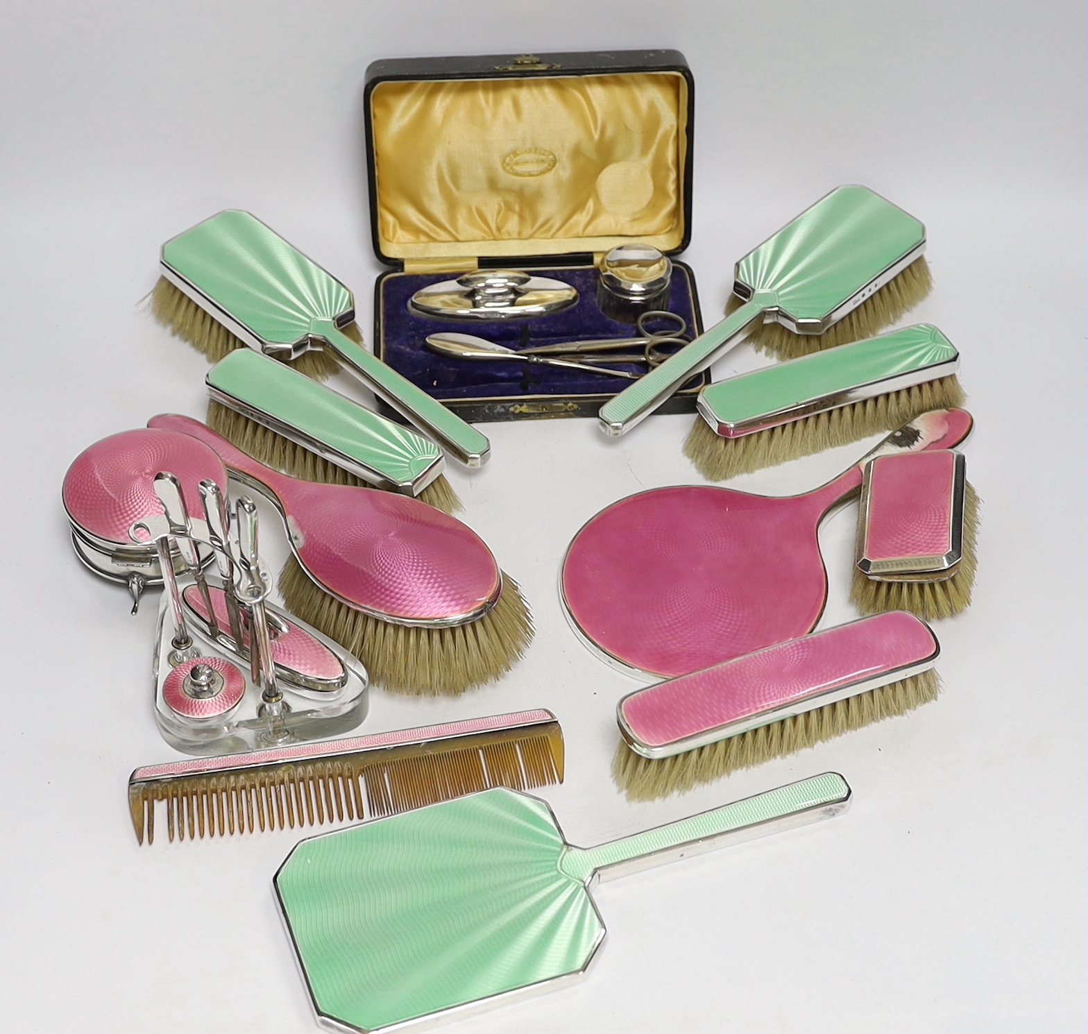 A 1930's five piece silver and green enamel mounted mirror and brush set by Mappin & Webb, a 1920's six piece silver and pink enamel mirror and brush set and two part manicure sets.